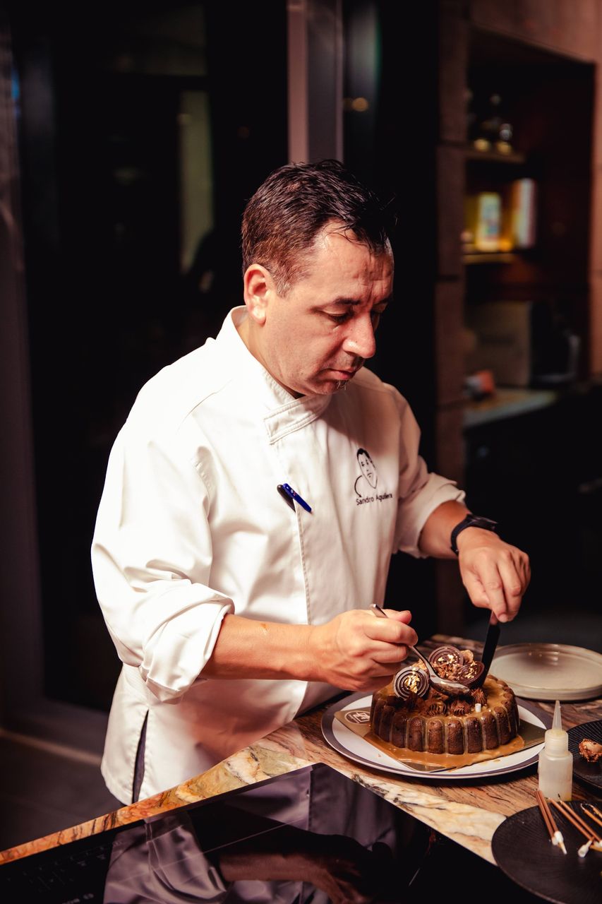 Chef Sandro Aguilera spooning a garnish onto a plated dessert