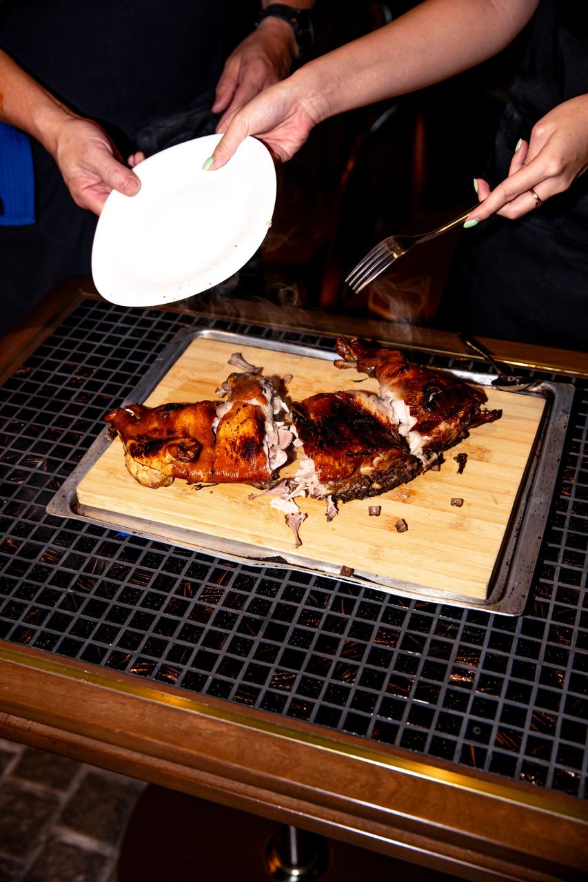 Whole roast suckling pig steaming on a wooden board as it is carved tableside