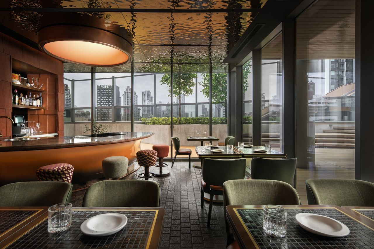 The dining room looking toward the curved copper bar, tables laid with green upholstered chairs