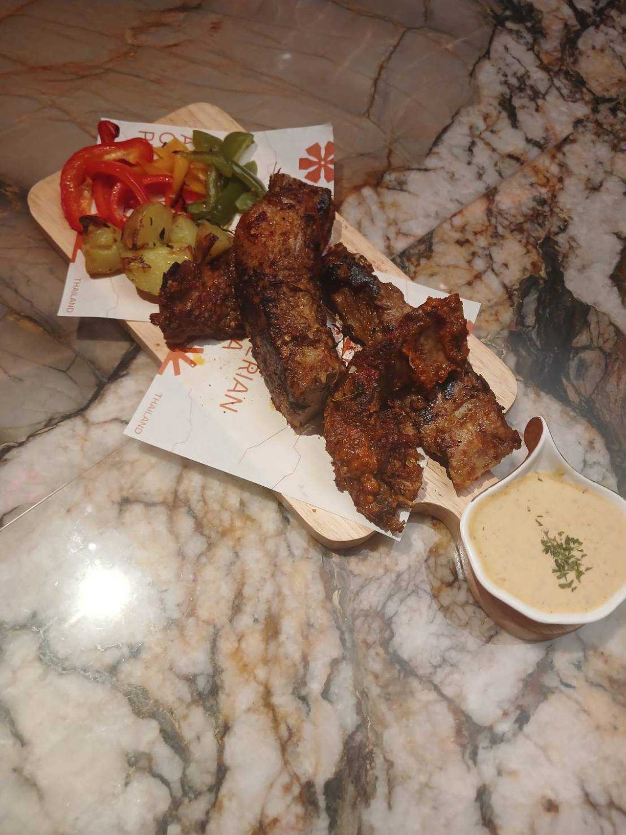 Roasted spiced pork spareribs on a wooden board with peppers, potatoes and a dipping sauce