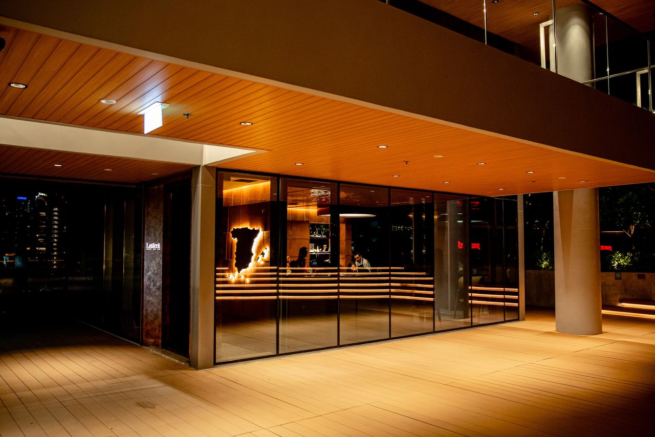 Latirra's glazed frontage lit at night beneath a timber-slatted soffit