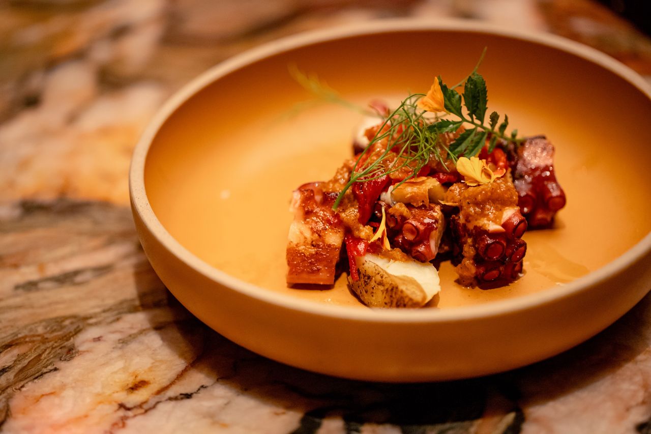 Charred octopus in a deep ochre bowl with crisp potato and paprika oil