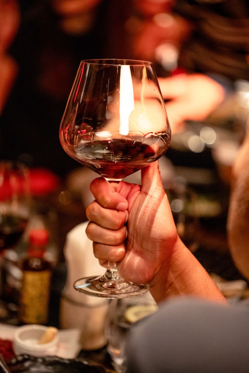 A balloon glass of red wine raised with a candle flame reflected in the bowl