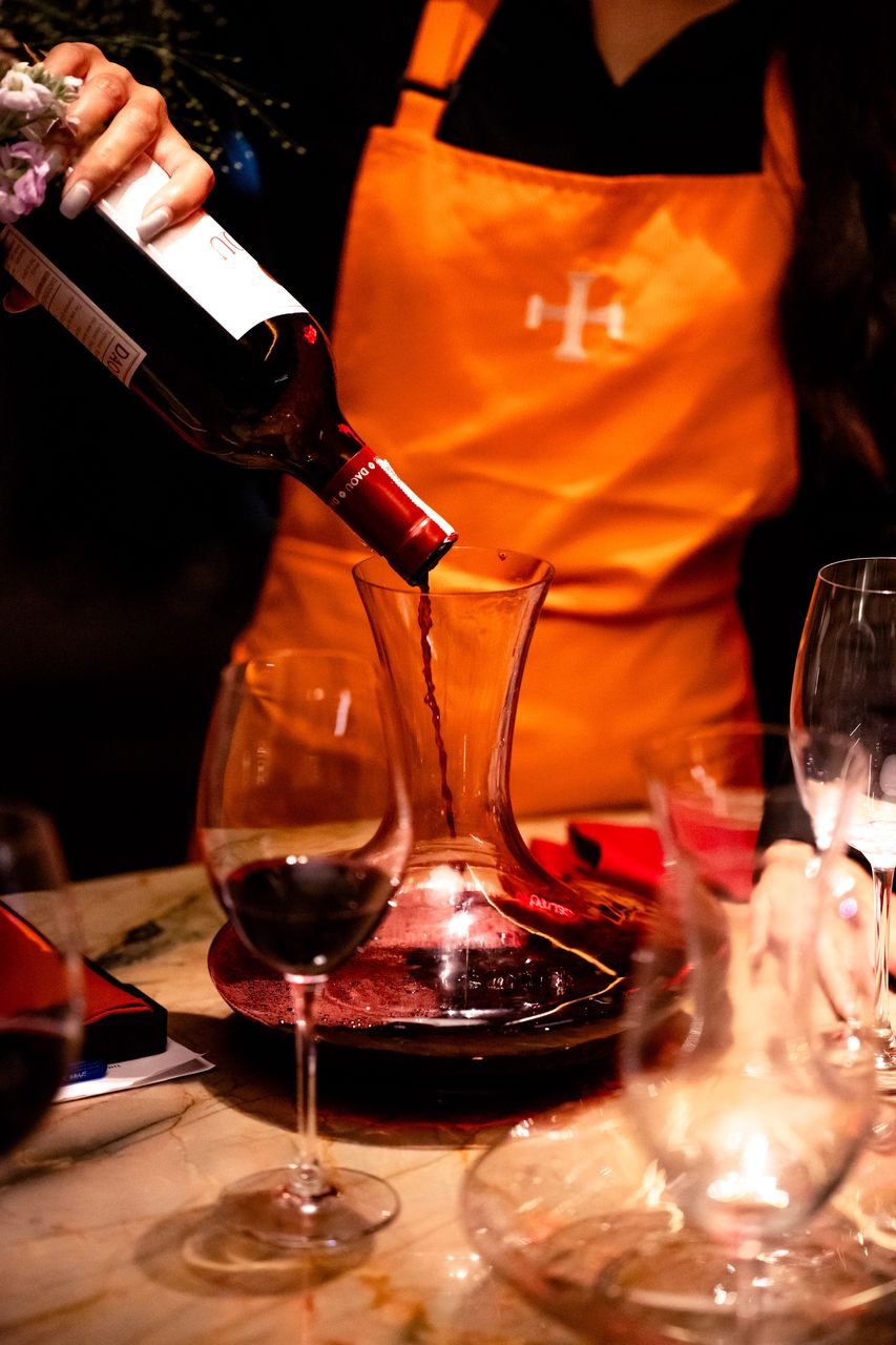 A member of the floor team decanting red wine into a glass decanter
